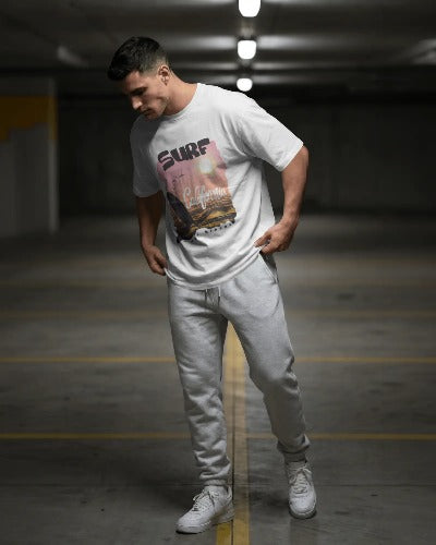 Man wearing a white t-shirt with a graphic design and light gray pants in an indoor setting.